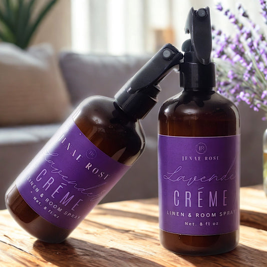 Two bottles of Lavender Creme by Tivoli Rose on a wooden surface with a vase of lavender in the background.